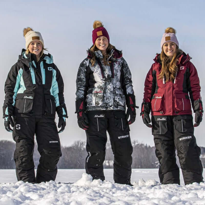 Three women in winter clothing standing on a snow-covered field with a clear sky.