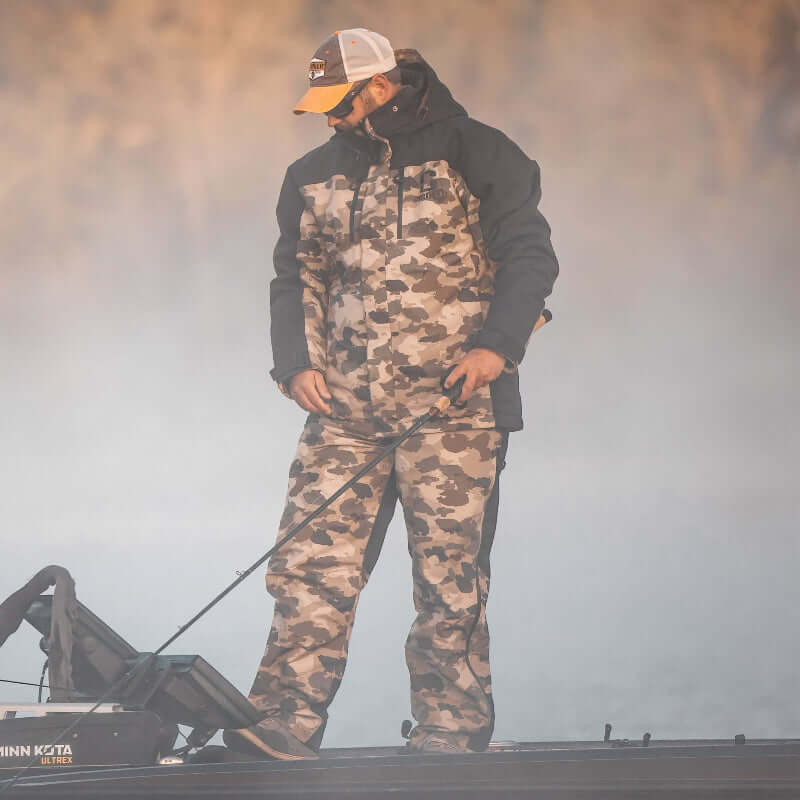 Person wearing camouflage overalls and a cap standing on a foggy background
