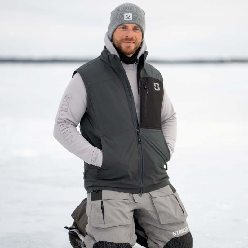 Man wearing a gray and black insulated vest with a brand logo, standing in a snowy landscape.