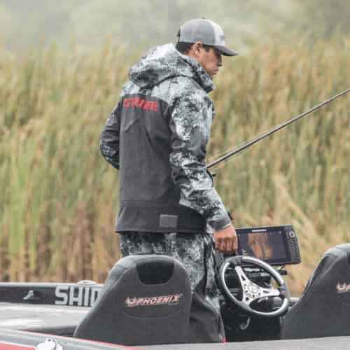 Man fishing from a boat wearing a camouflage jacket with 'Striker' branding.