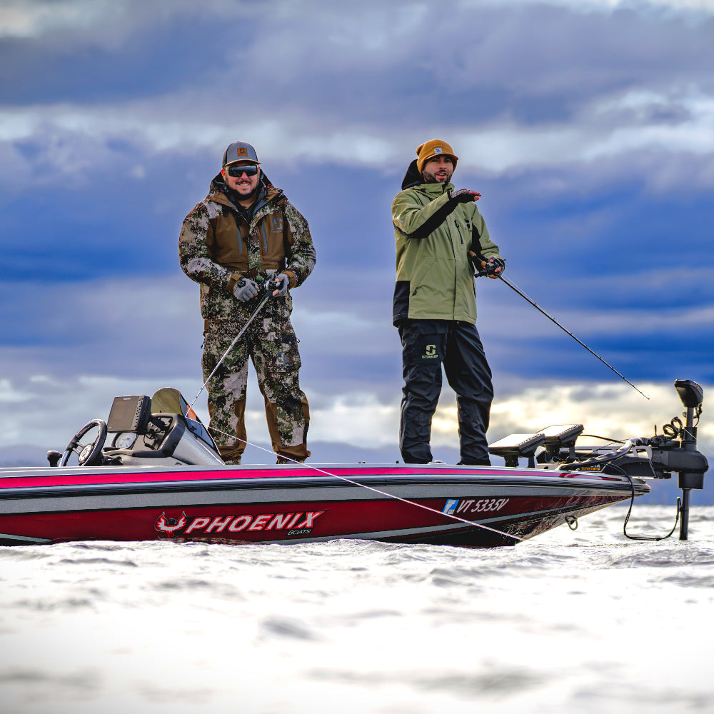 Two guys in Striker rain gear on a bass boat in a snowy landscape with a cloudy sky.