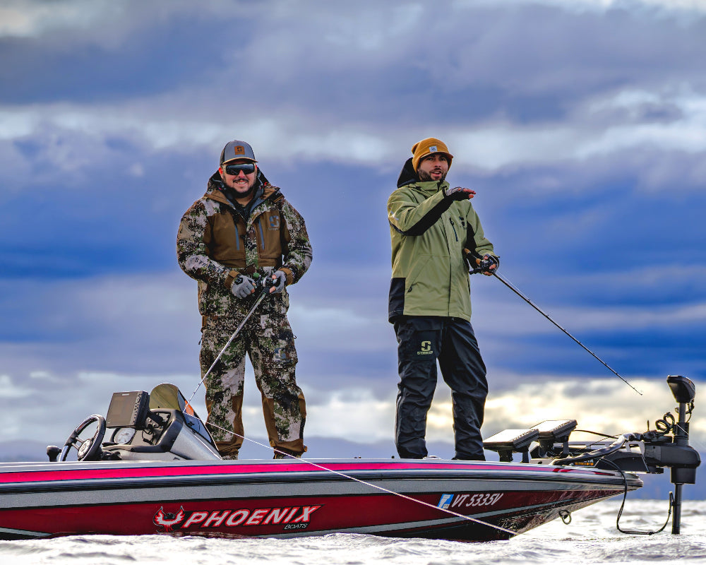 Two guys in Striker rain gear on a bass boat in a snowy landscape with a cloudy sky.