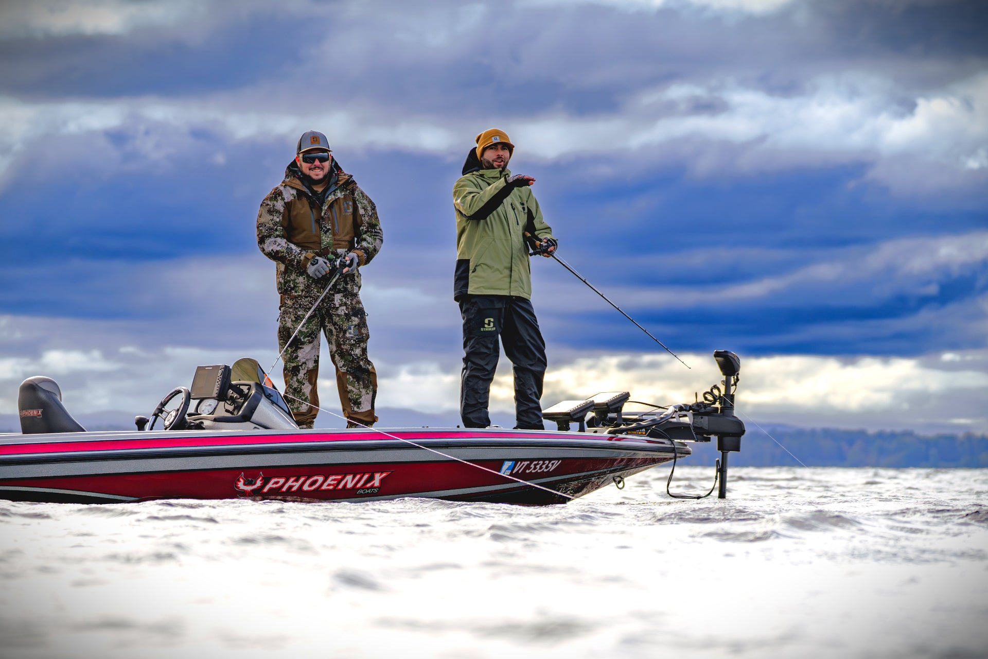 Two guys in Striker rain gear on a bass boat in a snowy landscape with a cloudy sky.