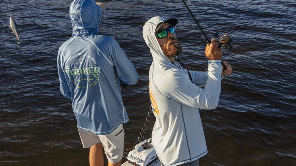 Two men fishing in the water, wearing hoodies with visible branding.