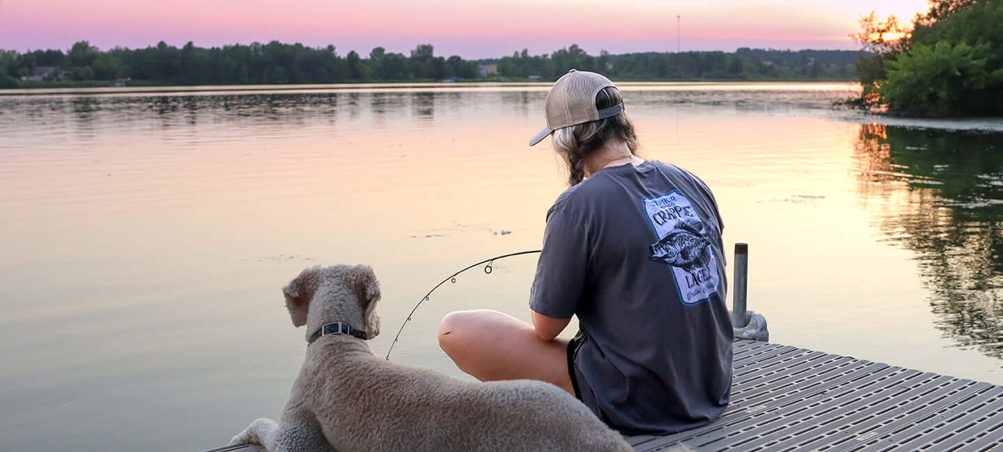 Woman and dog sitting at the dock fishing.
